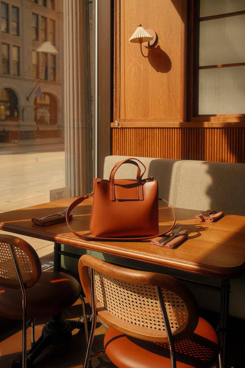 Image of a camel colored bag sitting on top of a table in a hip and trendy, empty, restaurant.